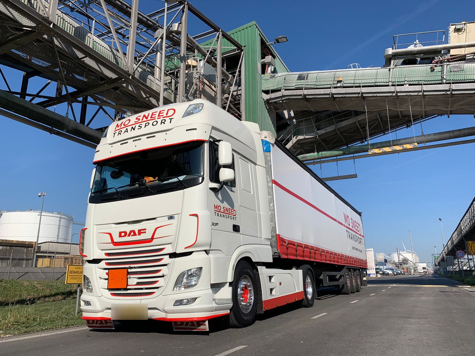 Een trekker met trailer onder een pijpbrug op een industrieterrein